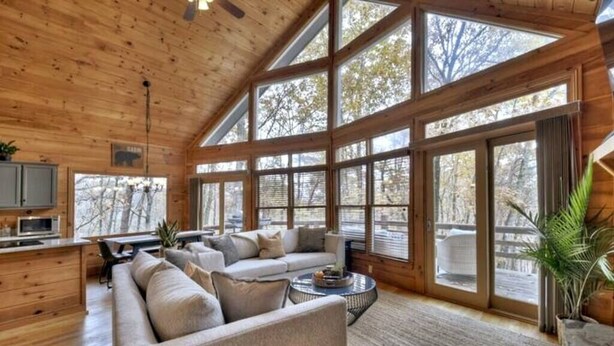A spacious cabin interior with a large sofa, a dining area, and a kitchen. - Lideca’s Treehouse | Hot Tub + Fire Pit + Games (Mineral Bluff)