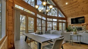 A cozy cabin interior with a dining area, sofa, and TV mounted on the wall. - Lideca’s Treehouse | Hot Tub + Fire Pit + Games (Mineral Bluff)