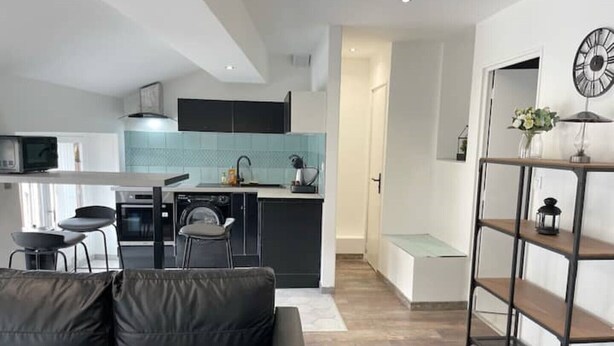 A modern kitchen with a central island, a dining area with a black leather couch, and a wooden floor. - 017 CHIC & COSY F2 53m2 HYPERCENTRE WIFI SMART TV NETFLIX (Saint-Étienne)