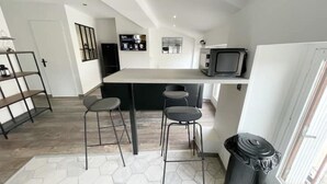 A modern kitchen with a central island, bar stools, a TV, and a trash bin. - 017 CHIC & COSY F2 53m2 HYPERCENTRE WIFI SMART TV NETFLIX (Saint-Étienne)