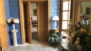 A hallway with a wooden door, a vase of flowers, a lamp, and a statue. - Chateau de la Mothe (Saint-Sulpice-en-Pareds)