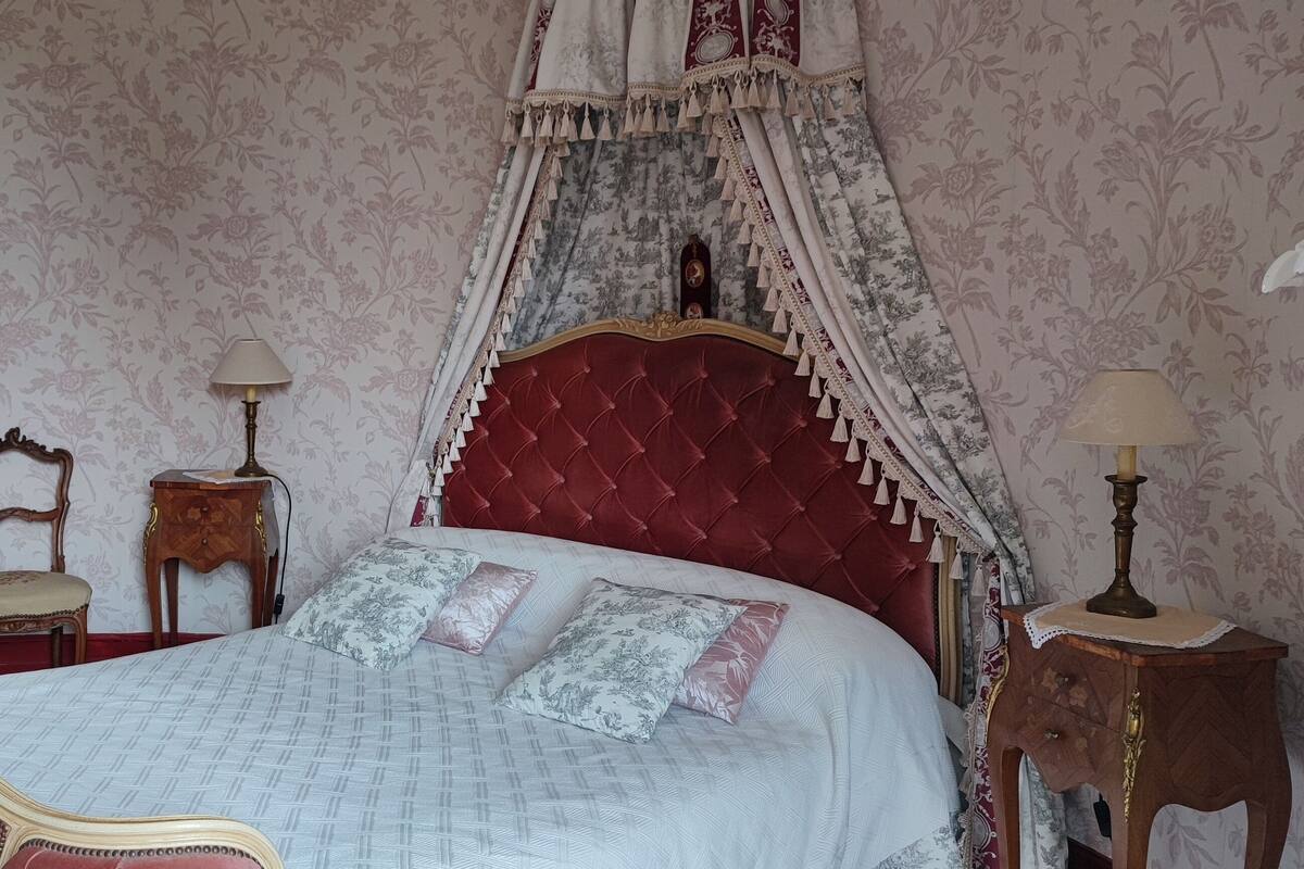 A bedroom with a large bed, a mirror, a chair, and a bedside table.