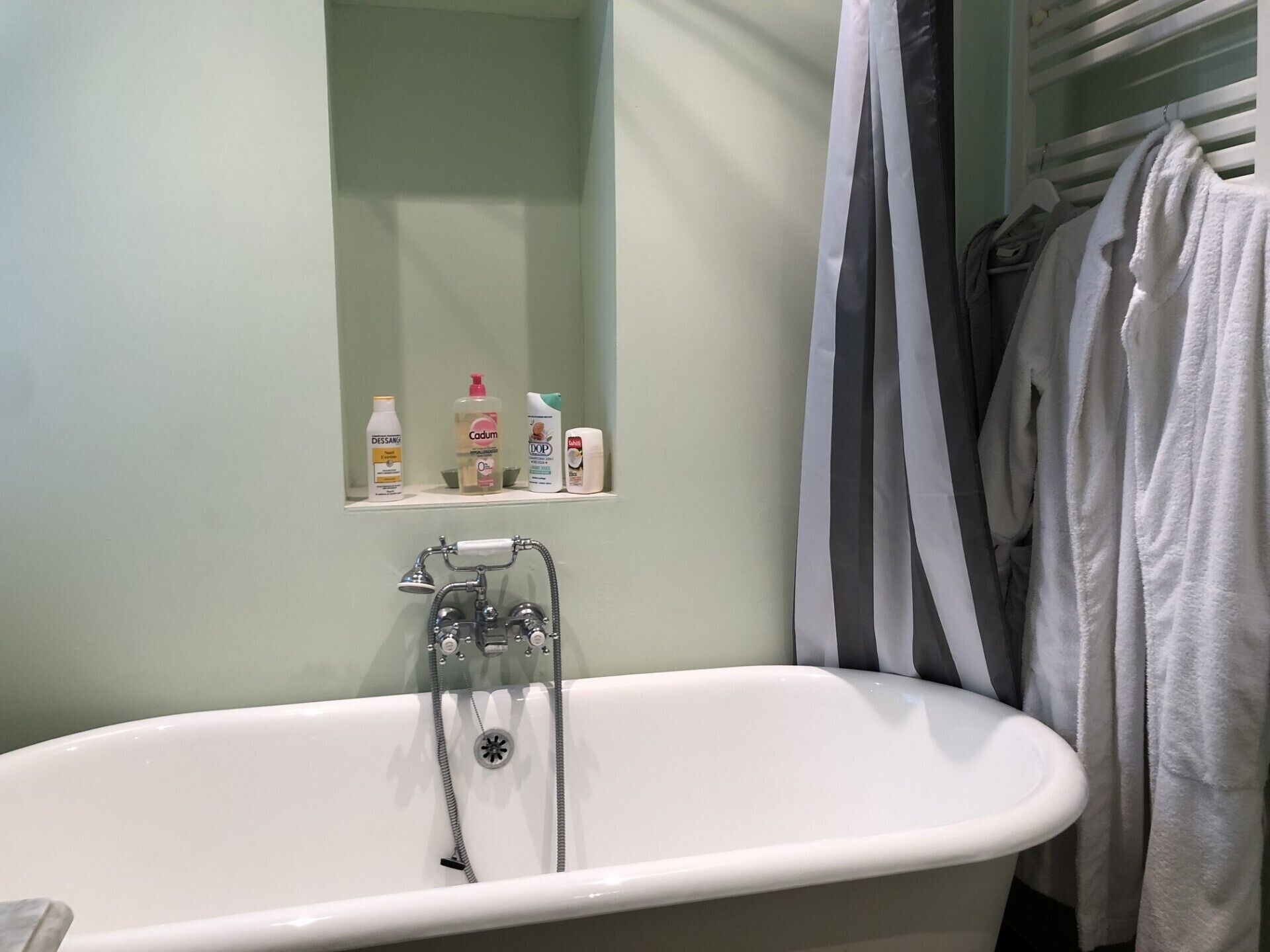 A bathroom with a white bathtub, a shelf with toiletries, and a towel rack with towels.