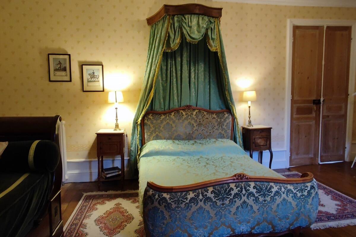 A bedroom with a four-poster bed, two bedside tables with lamps, a wardrobe, and a hanging clothes rack.