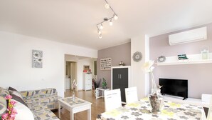A modern living room with a sofa, dining table, and TV. There is a bookshelf, a plant, and a vase with flowers. - Amelio, Apartment 5StarsHome Mallorca (Puerto Pollensa)