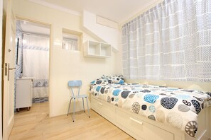 Quarto com cama, uma cadeira, um armário pequeno e janela com cortinas estampadas.
