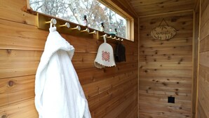 L'intérieur d'un chalet en bois, avec un banc en bois, une serviette accrochée au mur et une fenêtre donnant sur des arbres.