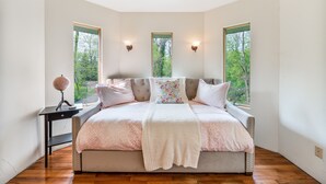 Une chambre à coucher avec un grand lit, deux fenêtres, une table de chevet et une lampe.