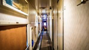 A narrow, metallic corridor with a central walkway, flanked by doors and windows, leading to a brightly lit area at the end. - Rail Hotel  (Galveston)
