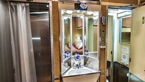 A compact, metallic bathroom with a sink, mirror, and a small window. - Rail Hotel  (Galveston)