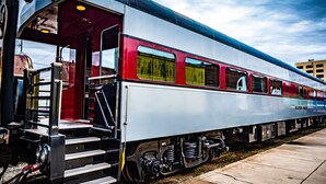 A stationary train with a metallic exterior, red and white color scheme, and a platform with steps leading to the train's entrance. - Rail Hotel  (Galveston)