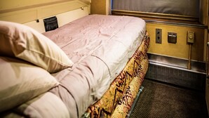 A narrow, single-bed room with a headboard, a window, and a small table. - Rail Hotel  (Galveston)