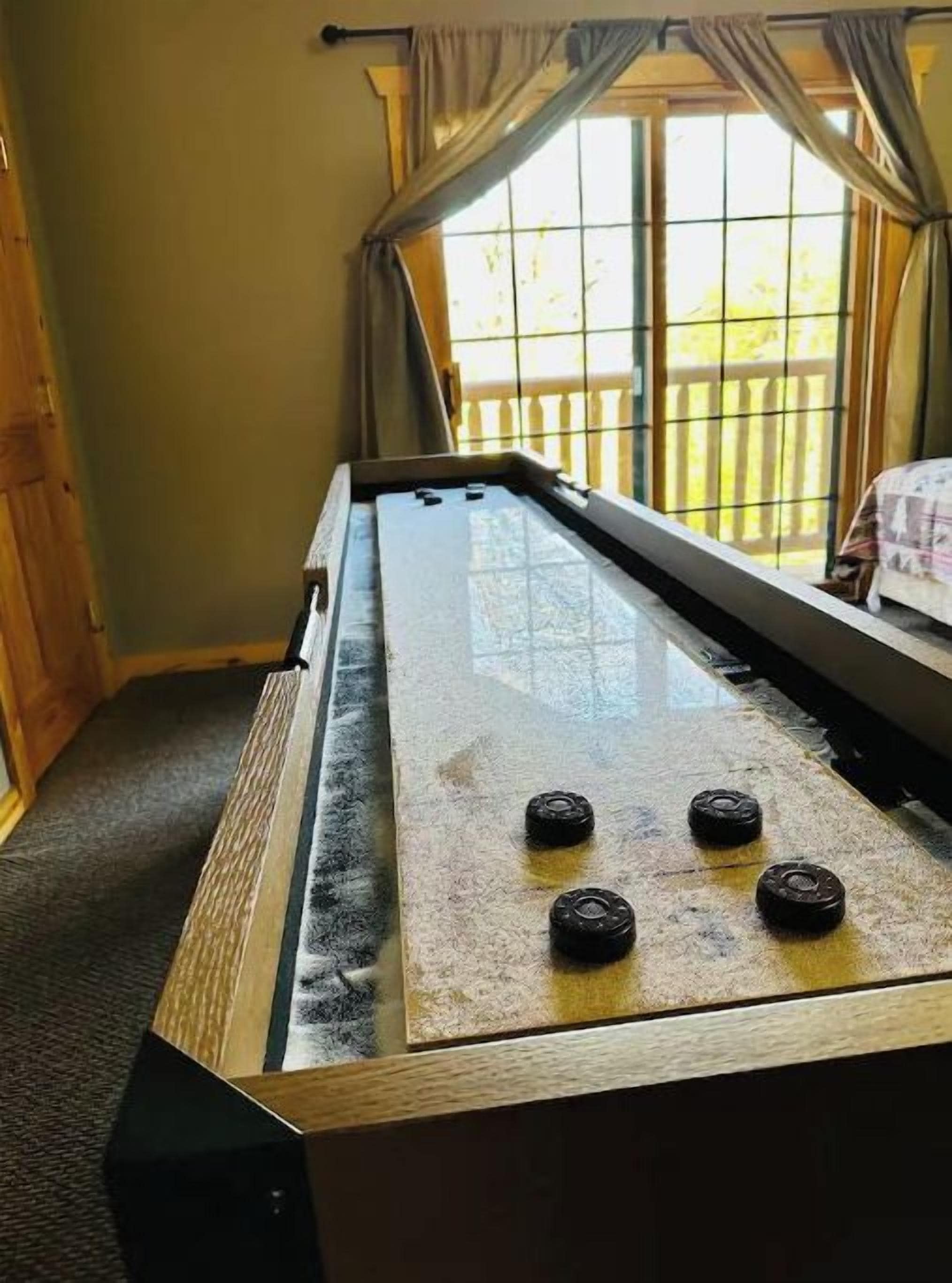 Una mesa de billar con superficie de vidrio y cuatro esquinas negras, ubicada en una habitación con ventana y cortinas.
