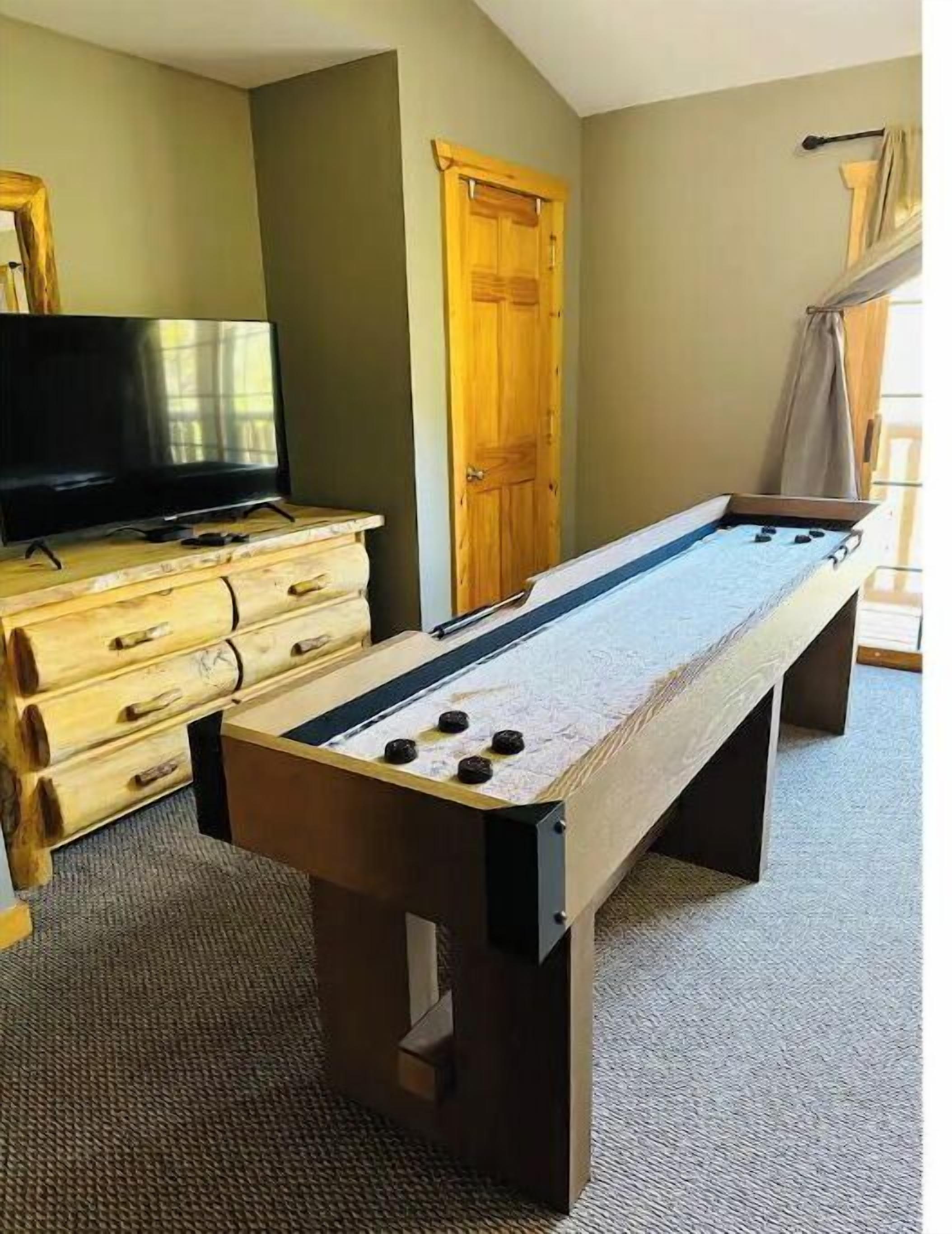 Una mesa de billar en una habitación con televisión, cómoda de madera y una puerta.