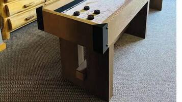 Una mesa de billar en una habitación con televisión, cómoda de madera y una puerta.