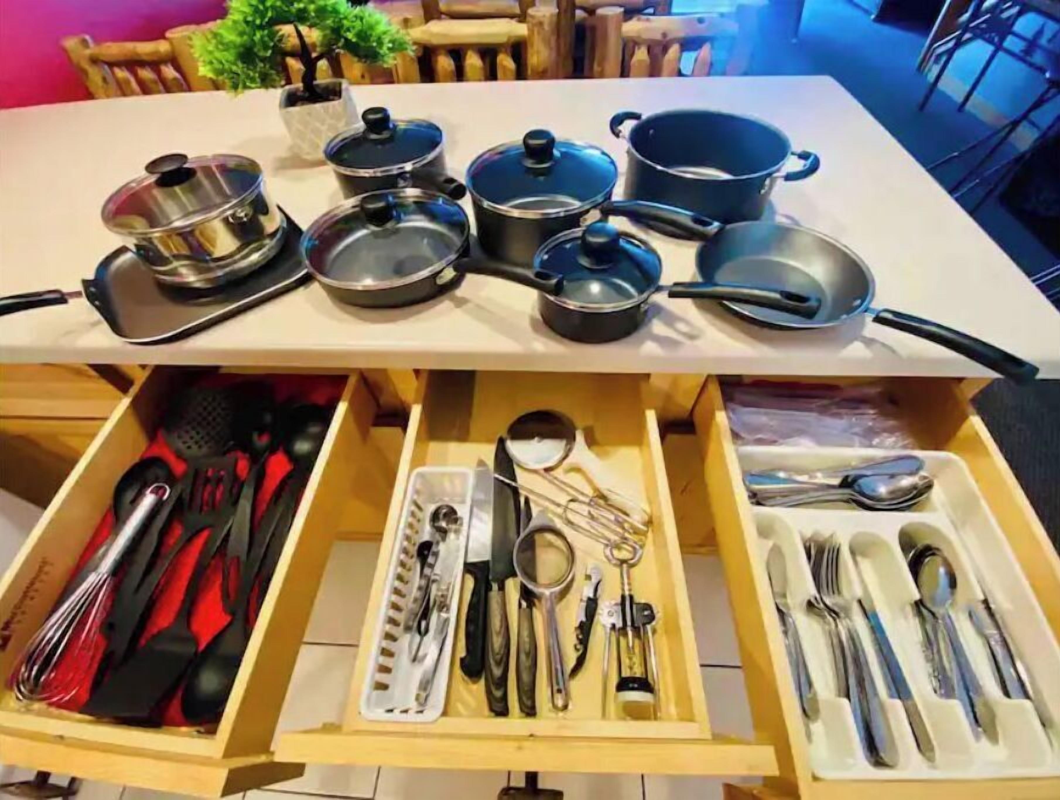 A kitchen with various pots and pans on the countertop and a drawer with utensils.