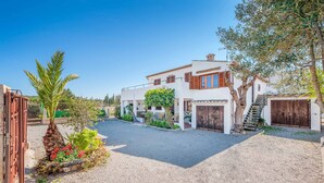 A modern house with a gravel driveway, a palm tree, and a garden with red flowers. - Palmestar, Finca 5StarsHome Mallorca (Puerto Pollensa)