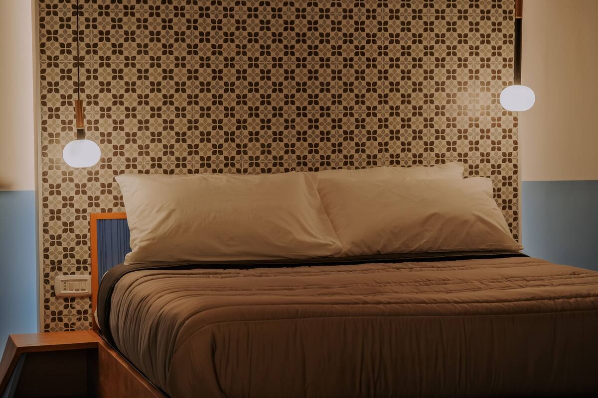 A neatly made bed with a patterned headboard, a bedside table, and a wall socket.