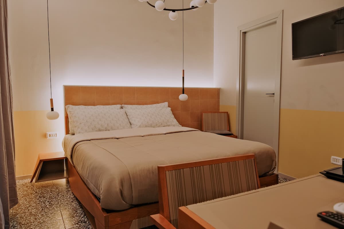 A hotel room with a bed, bedside table, lamp, TV, and a small table with a remote control.