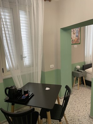 Une petite pièce avec une table et des chaises, un lit, une table de chevet et un tableau accroché au mur.