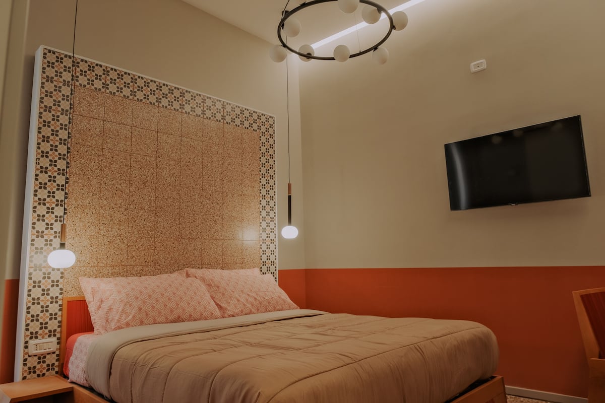 A bedroom with a bed, a television mounted on the wall, and a patterned headboard.