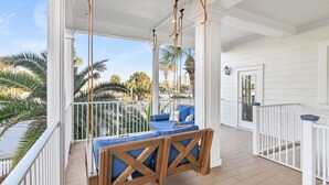 A covered porch with a swing set and seating area, overlooking a palm tree-lined street. - Private Pool & Spa Walk to 2 Beaches (Destin)