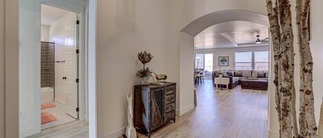 A spacious living area with a high ceiling, a wooden cabinet with decorative items, and a view into another room with a seating area.