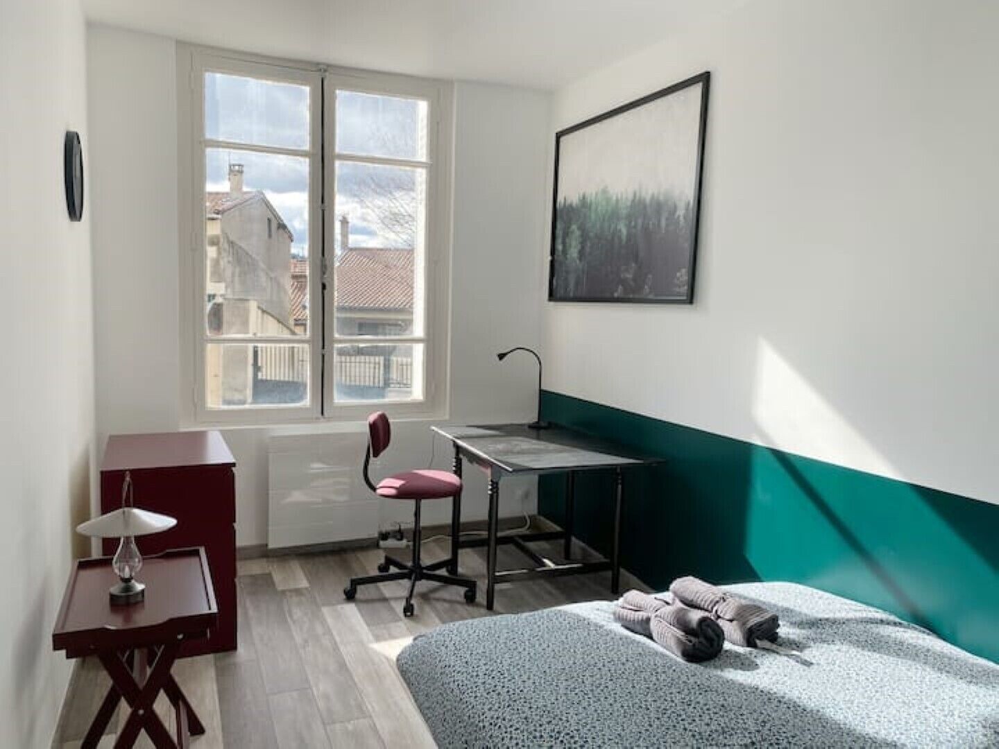 Ein Schlafzimmer mit Schreibtisch, Stuhl, Bett und einem Fenster mit Blick auf Gebäude.