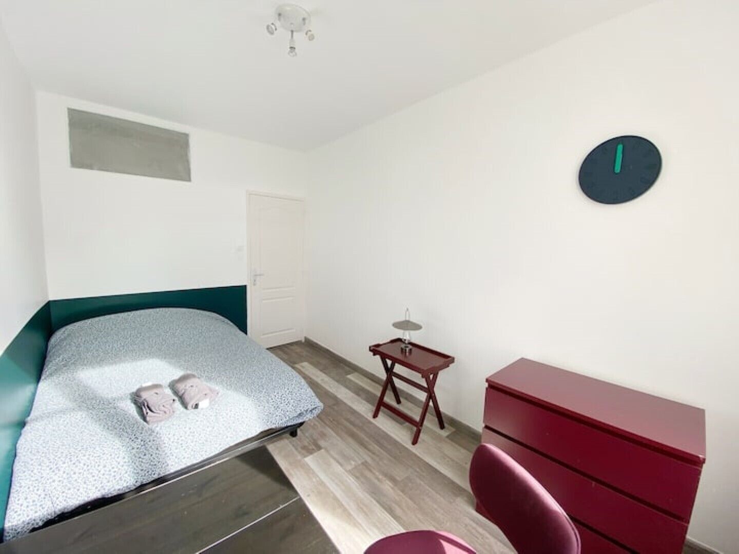 A bedroom with a bed, a desk, a chair, a dresser, and a wall clock.