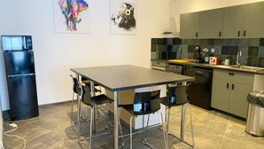 A modern kitchen with a dining table, chairs, a refrigerator, and artwork on the wall.