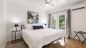 Un dormitorio con una cama grande, un ventilador de techo, una ventana con cortinas y un cuadro en la pared.
