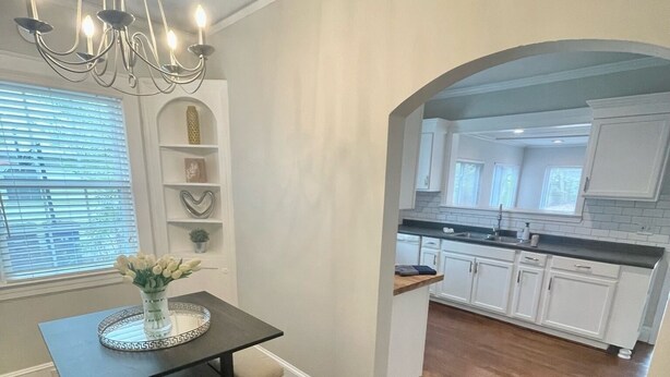 Een eetgedeelte met een tafel en stoelen, een kroonluchter en uitzicht op een keuken met witte kasten en een houten vloer.