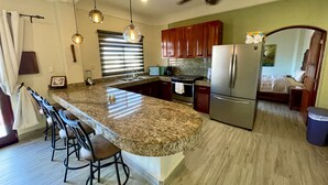 A kitchen with granite countertops, a refrigerator, and a dining area with bar stools. - Perfect Cozumel escape, pool, private beach on quiet north shore (San Miguel de Cozumel)