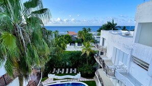 A pool surrounded by lush greenery and white buildings with balconies overlooking a beach. - Perfect Cozumel escape, pool, private beach on quiet north shore (San Miguel de Cozumel)