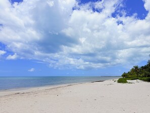 A beach with white sand, clear blue water, and scattered clouds.