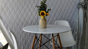 A small round table with a white chair and another chair with wooden legs. There is a vase with a sunflower on the table.