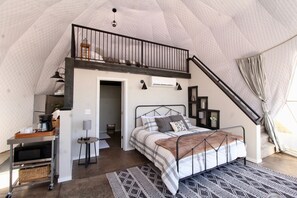 Un dormitorio con cama en altillo, un escritorio con cafetera y vistas al exterior.