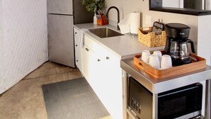 A compact kitchen with a refrigerator, sink, and a coffee maker on a cart.