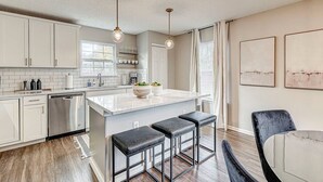 Una cocina moderna con armarios blancos, electrodomésticos de acero inoxidable, una isla de mármol y taburetes negros.