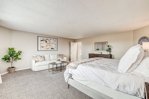 Une chambre à coucher avec un lit, un canapé blanc, une table basse, une plante en pot et un tableau accroché au mur.