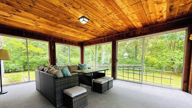 A cozy room with a wooden ceiling, large windows, a wicker sofa, and a table.