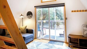 Une pièce de style loft avec un plafond en pente, un ventilateur de plafond, une grande porte-fenêtre coulissante donnant sur une terrasse, un canapé bleu et un tapis à motifs.