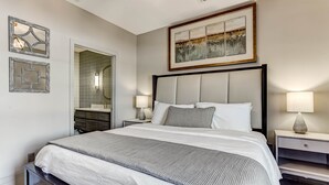 Un dormitorio ordenado con una cama grande, mesitas de noche, un espejo y cuadros en las paredes.