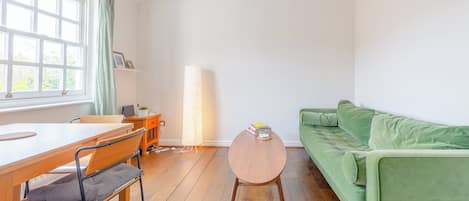 Une pièce avec une table en bois, un canapé vert, une lampe et une fenêtre avec des rideaux.