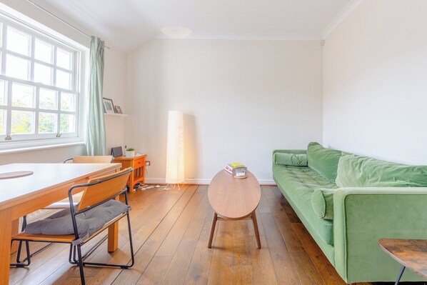 Une pièce avec une table en bois, un canapé vert, une lampe et une fenêtre avec des rideaux.