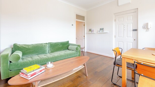 A room with a green sofa, a wooden table, and a chair. There are books on the table, and a door is visible in the background. - Peaceful 1BD Flat, 5 mins from Highbury &Islington (London)