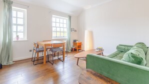 A room with a wooden dining table, two chairs, a green sofa, a small side table, and a window with curtains. - Peaceful 1BD Flat, 5 mins from Highbury &Islington (London)