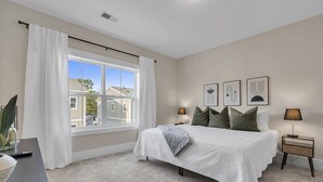 A bedroom with a bed, a nightstand, a lamp, a window with curtains, and framed pictures on the wall. - Downtown Greenville · 3BR/3.5BA · Private 2-Car Garage · Minutes to Main St (Greenville)