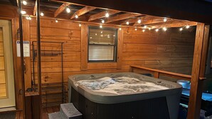 A hot tub in a wooden cabin with a window and string lights. - Naked Creek Cabin (Page County)