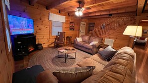 A cozy log cabin interior with a television, leather sofa, and a fireplace. - Naked Creek Cabin (Page County)